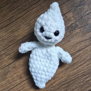 May include: A white crocheted ghost plush toy with black eyes and a smiling mouth. The ghost has a teardrop shape and is made with a fluffy yarn.