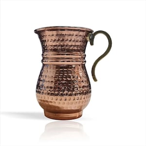 May include: A hammered copper jug with a brass handle. The jug has a rounded body and a wide mouth.