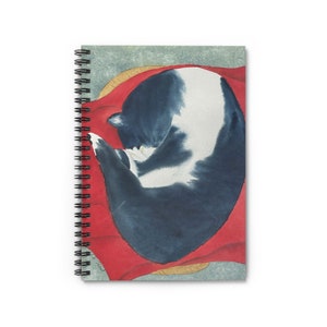 May include: A black and white cat curled up and sleeping on a red blanket. The cat is in a curled up position with its head tucked under its body. The blanket is a deep red colour and has a white border.