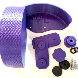 May include: A disassembled purple exercise wheel with a textured surface, a curved support, and various hardware components. The wheel has a geometric pattern. Additional parts include a knob, washers, and screws.