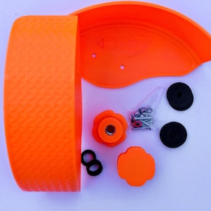 May include: An orange plastic wheel guard kit with various components. The kit includes a textured wheel guard, a curved shield, two black circular pads, two black O-rings, a flower-shaped knob, a four-leaf clover-shaped knob, and a bag of hardware.
