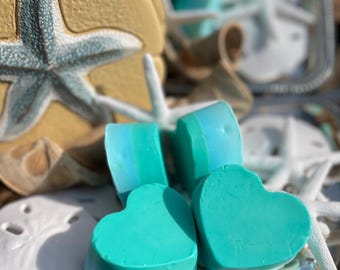 May include: Three teal blue heart-shaped soaps with a white stripe on each. The soaps are sitting on a silver tray with white seashells and starfish.