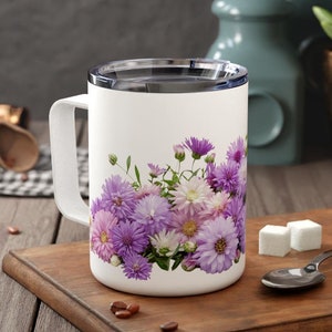May include: White ceramic mug with a purple and white floral design. The mug has a black lid and a handle.