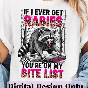 Puede incluir: Camiseta blanca con un diseño de mapache y el texto "If I Ever Get Rabies, You're On My Bite List". El mapache es negro y gris. Las palabras "Rabies" y "Bite List" tienen un diseño de estampado de leopardo.