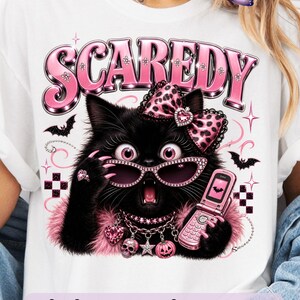 Bring a little drama and a lot of personality to your spooky season creations with this adorable Scaredy Cat Halloween PNG featuring a wide-eyed black cat in a glamorous pink coquette aesthetic. Dressed in sparkling rhinestone sunglasses, a pink leopard bow, layered jewelry, fluffy pink accents, and holding a trendy Y2K flip phone, this fashionable feline perfectly captures the playful side of Halloween.