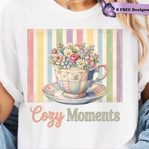 Könnte beinhalten: Ein weißes T-Shirt mit einer Grafik einer geblümten Teetasse auf einer Untertasse vor einem Hintergrund aus vertikalen Pastellstreifen. Unter der Tasse steht der Text Cozy Moments. Das Design enthält einen lila Schmetterling und 8 FREE DESIGNS INCLUDED.
