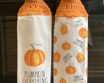 May include: Two white kitchen towels with orange crocheted tops and buttons. One towel has a single orange pumpkin with the text "Pumpkin Everything." The other towel has a repeating pattern of orange pumpkins with the text "Pumpkin Everything."