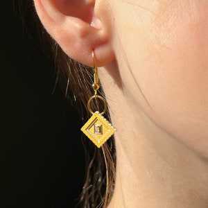 Op de afbeelding: Gouden oorbellen met een gele diamantvormige hanger. De hanger heeft een kleinere diamant in het midden.
