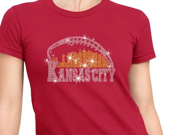 May include: Red t-shirt with a rhinestone design of the Kansas City skyline and a football. The text "KANSAS CITY" is spelled out in rhinestones.