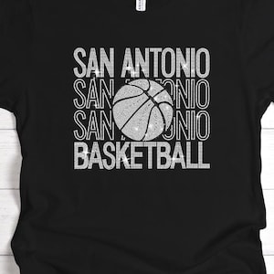 May include: Black t-shirt with the words "SAN ANTONIO" stacked vertically three times, with a basketball graphic in the center. The word "BASKETBALL" is printed below the basketball. The text and graphic are in white.