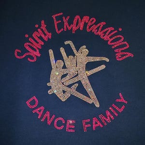 Op de afbeelding: Een marineblauw t-shirt met een strass-ontwerp van drie dansende figuren in het midden. De tekst "Spirit Expressions" is boven de figuren gebogen en "DANCE FAMILY" eronder, allemaal gemaakt van roze en doorzichtige strass-steentjes.