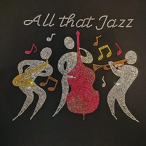 Peut inclure: T-shirt noir avec l'inscription "All that Jazz" en strass. Le motif repr&eacute;sente des personnages en strass jouant d'instruments de musique, dont une guitare, une contrebasse et une trompette, avec des notes de musique.