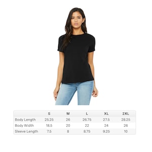 May include: A black short-sleeve t-shirt. The image includes a size chart with measurements in inches for body length, body width, and sleeve length for sizes S, M, L, XL, and 2XL. The model is wearing blue jeans.