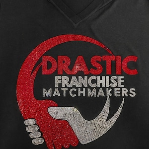 Peut inclure: T-shirt noir &agrave; col en V avec un motif en strass. Le motif pr&eacute;sente le mot "DRASTIC" en strass rouges et les mots "FRANCHISE MATCHMAKERS" en strass argent&eacute;s, ainsi qu'un graphisme rouge et argent.