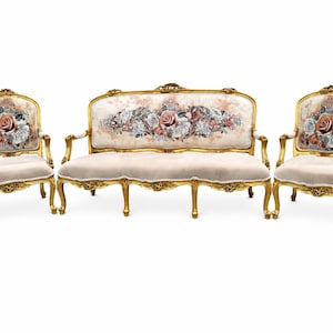 May include: A three-piece furniture set consisting of one sofa and two armchairs. Each piece features a gold-painted wooden frame with ornate carvings, light beige velvet upholstery, and a floral rose pattern on the backrests.