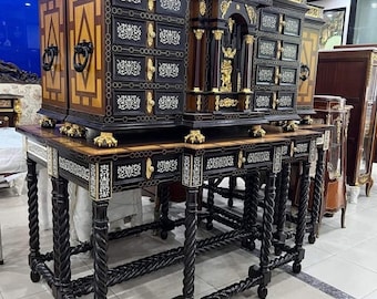 May include: A black and gold antique cabinet with intricate carvings and inlays. The cabinet has multiple drawers and doors, and is supported by four turned legs. The cabinet is displayed on a white tiled floor.