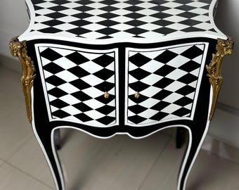 May include: A black and white checkered end table with gold accents and curved legs. The table has two doors and a top surface with a checkered pattern.