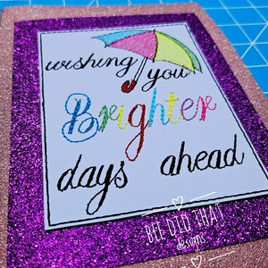May include: A pink and purple glitter card with a white card insert. The insert has a colorful rainbow umbrella and the text "Wishing you brighter days ahead". The bottom of the card has the text "Bee Did That Designs".