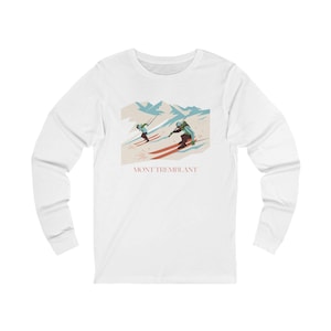 Op de afbeelding: Wit shirt met lange mouwen met een afbeelding van twee skiërs op een berghelling. De illustratie bevat de tekst "MONT TREMBLANT" in roodbruin. Het ontwerp is tegen een achtergrond van besneeuwde bergen.