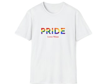 Op de afbeelding: Wit t-shirt met het woord "PRIDE" in regenboogkleuren over de borst. Onder het woord "PRIDE" staat de zin "Love Wins" in het rood. Het shirt heeft een ronde hals.