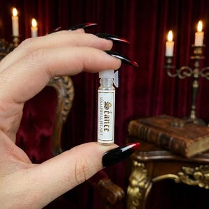 May include: A small, clear glass vial with a white plastic stopper and a rectangular white label. The label features the text 'S&eacute;ance' in a decorative font above the words 'VAMPRESS HEART' in a simple, capitalized sans-serif typeface.