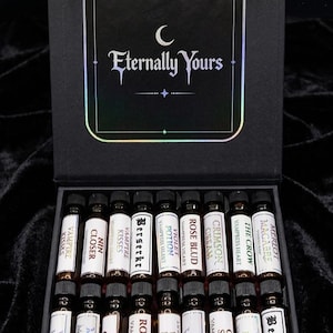May include: A black rectangular box containing sixteen small glass vials with black caps. Each vial features a white label with text including names like Berserker, Rose Blud, and Crimson Cream. The box lid displays the text Eternally Yours in white.