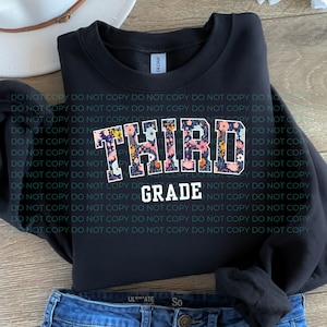 May include: A black long-sleeve sweatshirt featuring the word THIRD in a collegiate font filled with a colorful floral pattern of pink, orange, and white flowers on a dark background, with the word GRADE printed below in plain white letters.