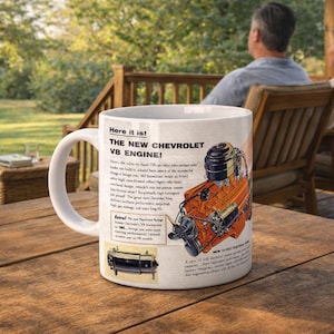 May include: White ceramic mug featuring a vintage advertisement for the new Chevrolet V8 engine. The mug displays an illustration of the engine in orange and black, with accompanying text. The mug is on a wooden table.
