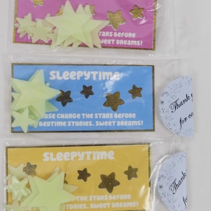 May include: Three packages of glow-in-the-dark stars for kids. Each package has a different colored background: pink, blue, and yellow. The packages say "Sleepytime" and have instructions to charge the stars before bedtime.