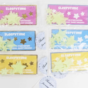 May include: Four packages of glow-in-the-dark star stickers. Each package has a blue, yellow, or pink background with the text "Sleepytime" and "The stars before stories, sweet dreams!" The packages are sealed in clear plastic.