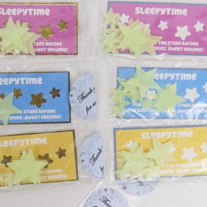 May include: Four packages of glow-in-the-dark star stickers. Each package has a blue, yellow, or pink background with the text "Sleepytime" and "The stars before stories. Sweet dreams!" The packages are sealed in clear plastic.