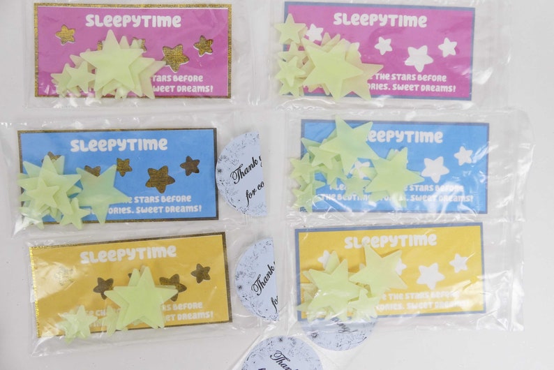 May include: Four packages of glow-in-the-dark star stickers. Each package has a blue, yellow, or pink background with the text "Sleepytime" and "The stars before stories. Sweet dreams!" The packages are sealed in clear plastic.