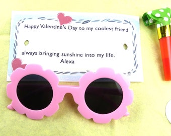 Könnte beinhalten: Rosa-farbene Sonnenbrille in Blumenform mit schwarzen Gläsern und einer Valentinstagskarte mit dem Text "Happy Valentine's Day to my coolest friend always bringing sunshine into my life. Alexa"