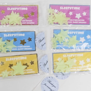 May include: Four packages of glow-in-the-dark star stickers with a yellow, blue, pink, and light blue background. Each package has the text "Sleepytime" and "The stars before stories. Sweet dreams!" printed on it.