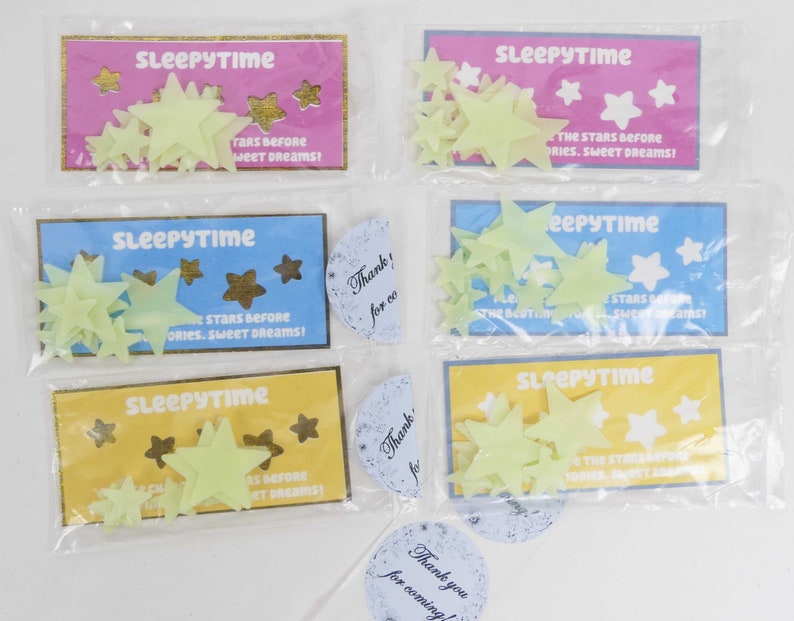 May include: Four packages of glow-in-the-dark star stickers with a yellow, blue, pink, and light blue background. Each package has the text "Sleepytime" and "The stars before stories. Sweet dreams!" printed on it.