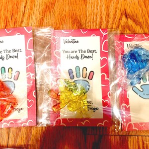 May include: Three Valentine's Day cards with hand-shaped sweets and the message "You are The Best. Hands Down!" The cards are pink with hearts and the sweets are orange, yellow, and blue.