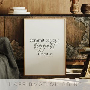 Könnte beinhalten: Gerahmter Druck mit dem Schriftzug "commit to your biggest dreams" in stilvoller Schrift. Der Druck hat einen neutralen Hintergrund und einen hellen Holzrahmen. Der Text "1 Affirmation Print" befindet sich unten.