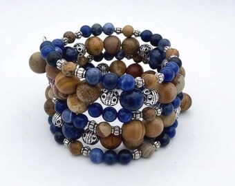 Puede incluir: Una pulsera de varias vueltas con cuentas redondas alternas en tonos azul profundo, bronceado y marrón. El diseño incorpora pequeñas cuentas espaciadoras de metal plateado texturizado entre las esferas, creando una apariencia en capas.