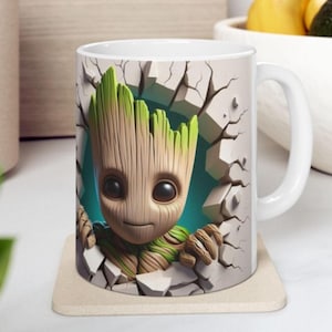 May include: White ceramic mug featuring a cartoon character breaking through a wall. The character has a wooden appearance with green leaves on top. The mug has a white handle and is sitting on a beige coaster.