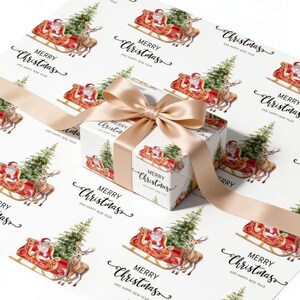 May include: A white gift box wrapped in paper featuring a repeating watercolour pattern of Santa Claus in a red sleigh pulled by a reindeer, with green pine trees and the text Merry Christmas and happy new year, tied with a beige satin ribbon.