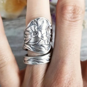 May include: A silver spoon ring featuring a floral design. The ring is crafted from a vintage spoon and wraps around the finger.