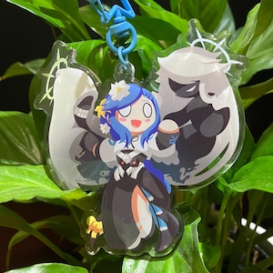 May include: A clear acrylic keychain featuring a cartoon character with blue hair, a white dress, and a black and white creature behind her. The keychain has a blue star-shaped charm attached to it.