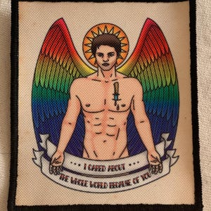 May include: A rectangular patch with a black border features a shirtless figure with rainbow wings and a halo. A dagger is depicted on the chest. The text on a banner reads "I CARED ABOUT THE WHOLE WORLD BECAUSE OF YOU."
