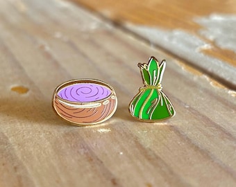 May include: Two enamel pins, one depicting a purple and pink swirl in a brown bowl, the other a green and gold pouch.