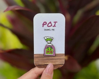 May include: A purple and green enamel pin of a bag of poi, a traditional Hawaiian food. The pin says "POI" on the bag.