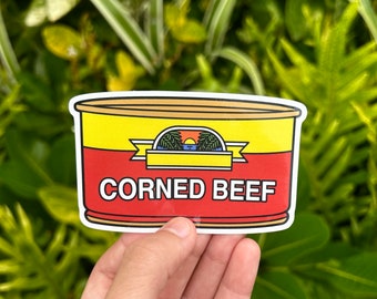 May include: A sticker of a yellow and red can of corned beef with a palm tree and sunset graphic. The can says "Corned Beef" in bold black letters.