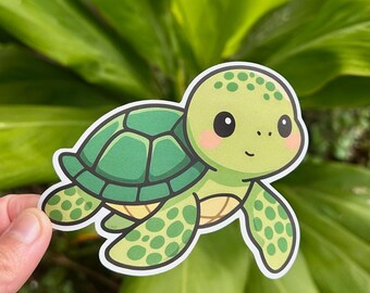 May include: A green turtle sticker with a cartoon design. The turtle has a green shell, light green head and limbs, and a smiling face. The sticker is held in front of a background of green leaves.