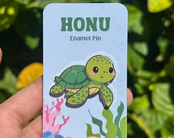 May include: A light blue enamel pin featuring a cartoon turtle with a green shell and a smiling face. The pin is labeled "HONU" with the words "Enamel Pin" below. The background includes coral and seaweed.