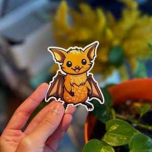 May include: A sticker of a cartoon bat with orange fur and brown wings. The bat has a happy expression and is standing on its hind legs.