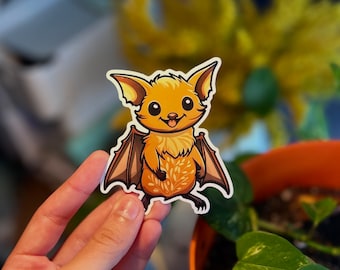 May include: A sticker of a cartoon bat with orange fur and brown wings. The bat has a happy expression and is standing on its hind legs.